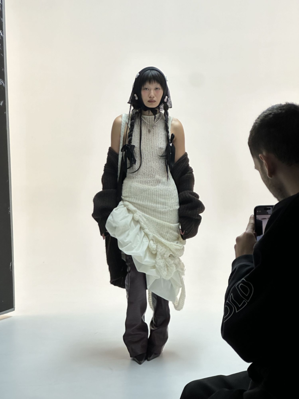 Ein Model in weißem, strukturiertem Kleid mit futuristischen Details, umgeben von minimalistischer Studioatmosphäre.  Fokus auf Exosoziologie, Science-Fiction, Zukunftsvisionen.