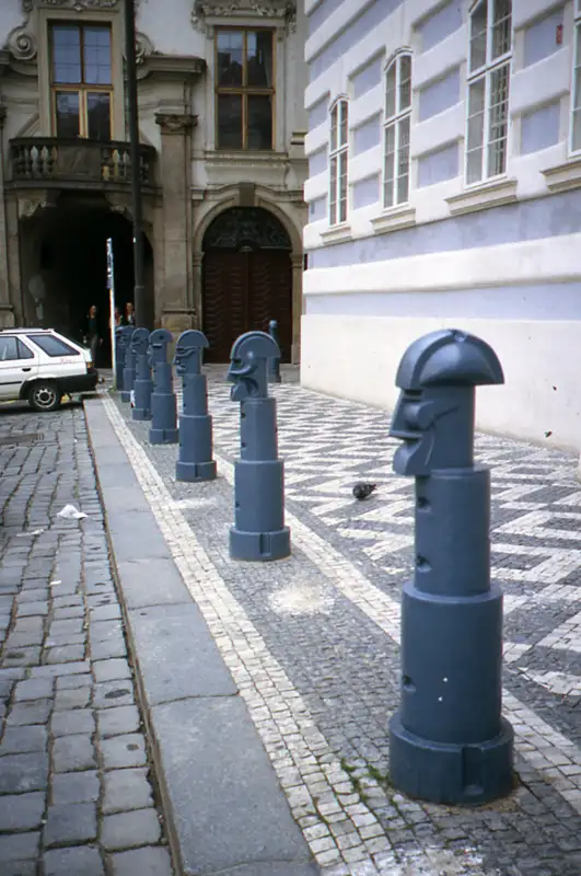 Eine Reihe von skulptural gestalteten Pollern mit Gesichtern steht entlang einer gepflasterten Straße, ein kreatives Beispiel für städtische Pollerforschung und Design.